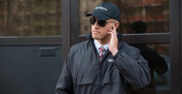 Vigilante patrimonial atento com uniforme preto em frente a prédio.